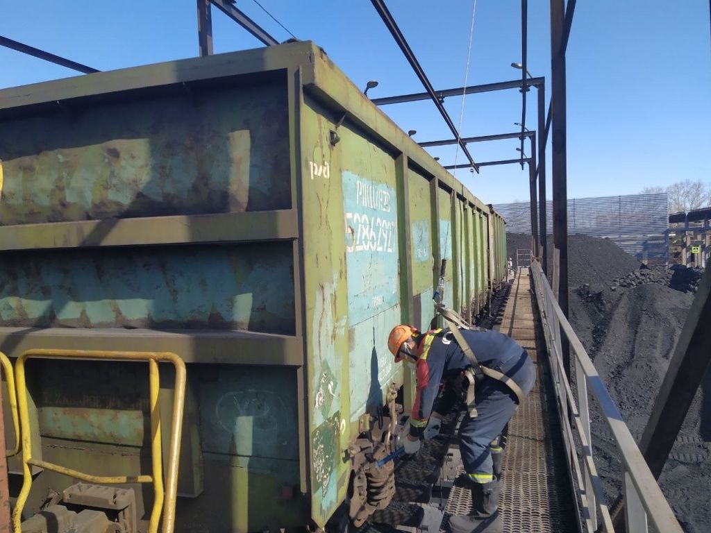 На эстакаде с помощью кувалды специалист открывает нижние выгрузочные люка полувагона