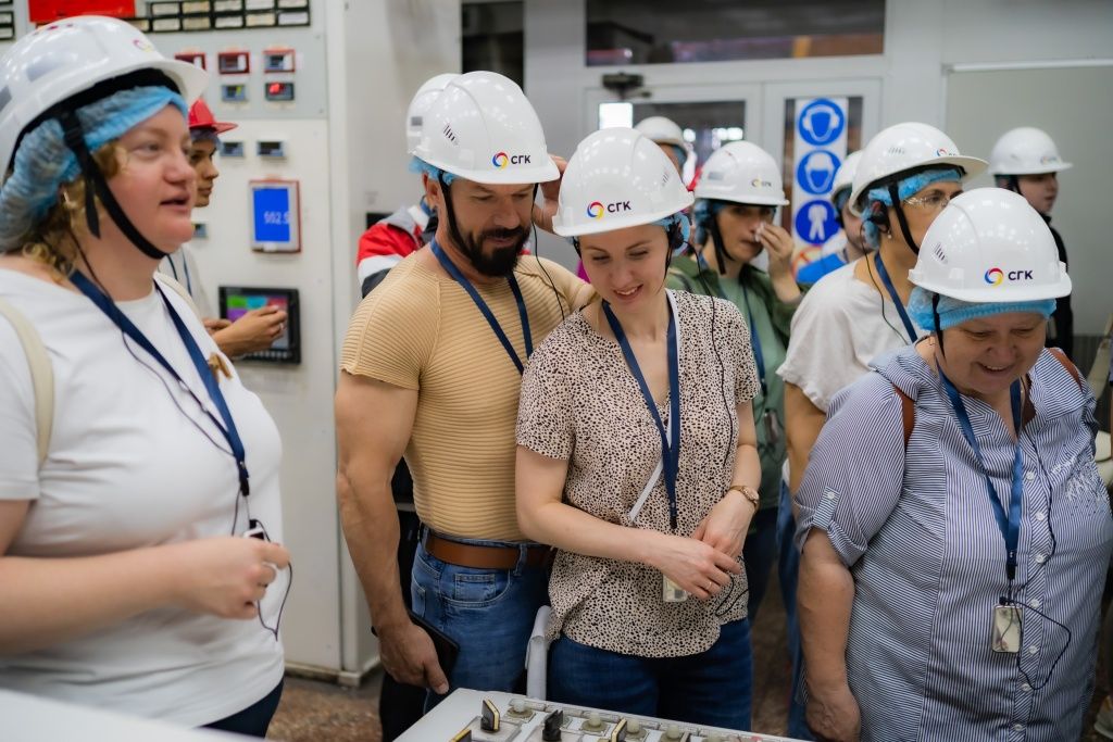 Экскурсанты изучают оборудование и слушают гида во время экскурсии. На заднем фоне &mdash; как раз привлекшие внимание знаки безопасности 