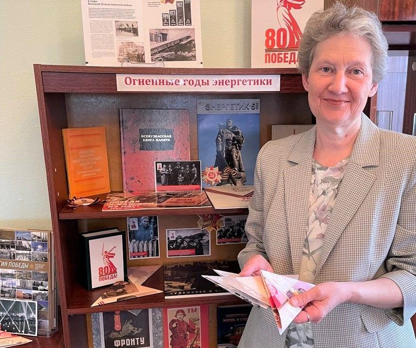 Марина Беляева на фоне выставки. В руках &mdash; конверты с биографиями ветеранов-энергетиков